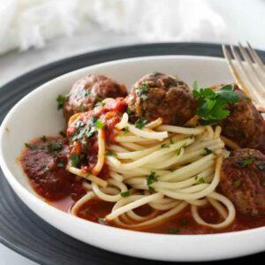 Spaghetti with tomato sauce and meatballs in a white bowl, fork beside.