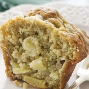 Sliced apple muffin with glaze on a white plate beside a fork.