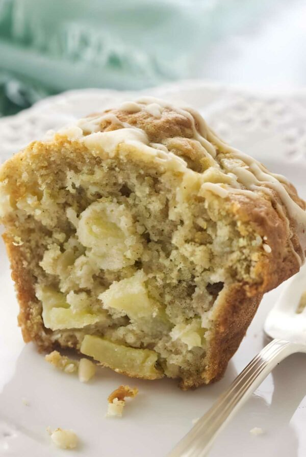 Sliced apple muffin with glaze on a white plate beside a fork.