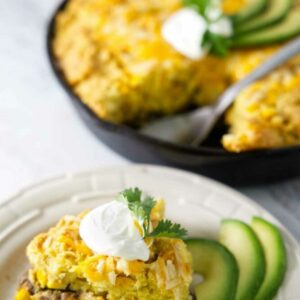 Cornbread casserole slice with sour cream, cilantro, and avocado on a plate.
