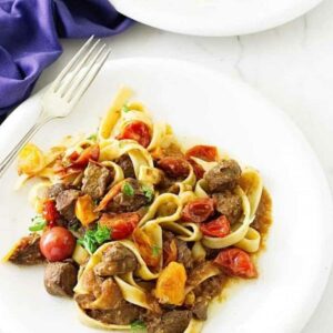 Pasta with beef, tomatoes, and herbs on a white plate with fork.