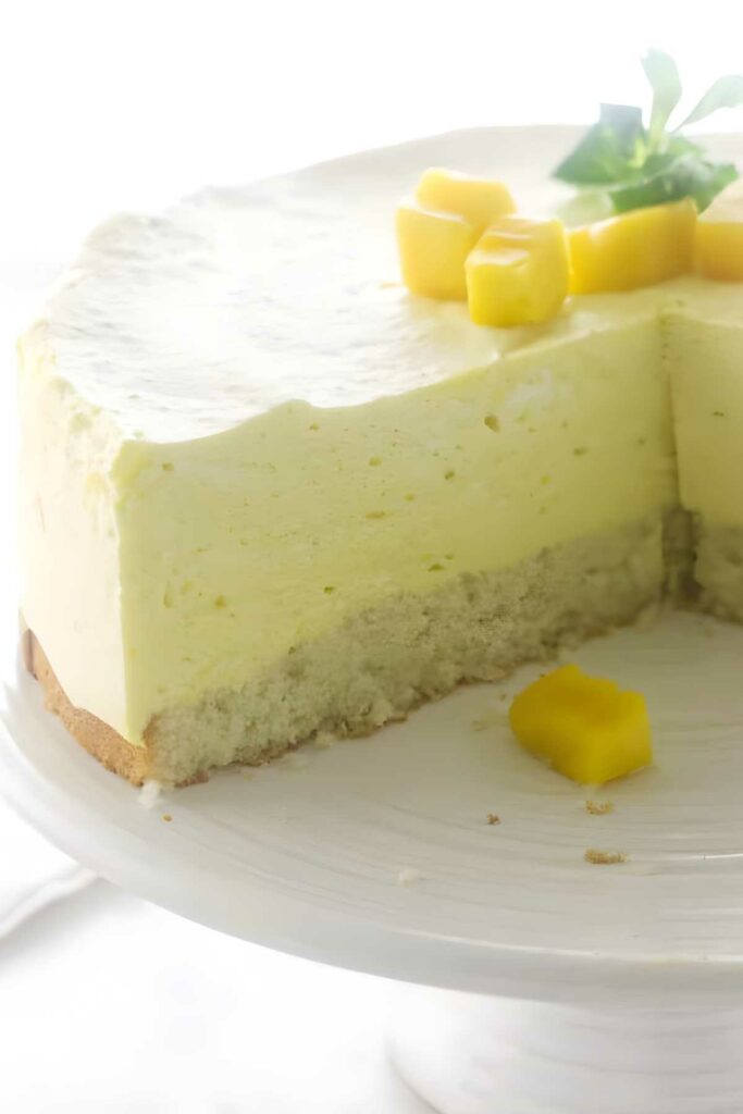 Mango mousse cake with whipped cream and cubes, slice showing mousse layers.