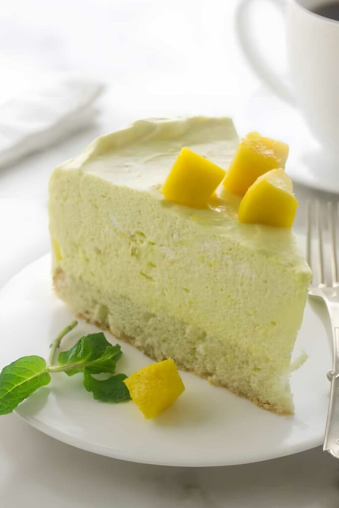 Slice of mango mousse cake with fresh mango and mint on a white plate.