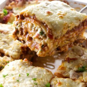Cheesy lasagna slice lifted from dish, layers and parsley visible.