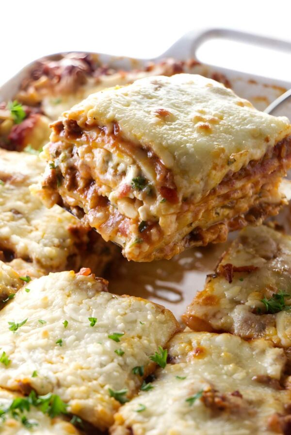 Cheesy lasagna slice lifted from dish, layers and parsley visible.