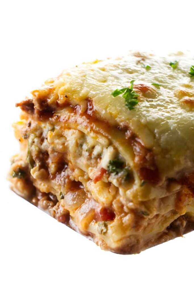 Lasagna slice with cheese, herbs, and parsley on a white background.