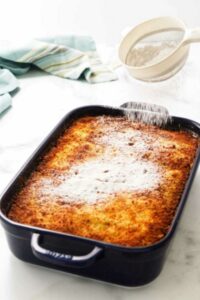 Blue baking dish with monte cristo casserole being dusted with powdered sugar.