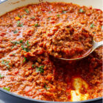 A spoon scooping a serving of ragu bolognese sauce.