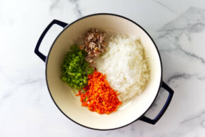 Adding bacon and diced veggies to a large skillet.