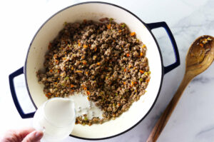 Pouring cream into the pot with the browned meat.