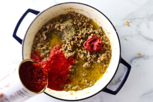 Adding crushed tomatoes to the browned beef and pork.