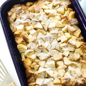 French toast bake with apples in a rectangular dish beside a metal spatula.