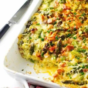 Baked casserole with asparagus, cheese, and ham in white dish on marble.