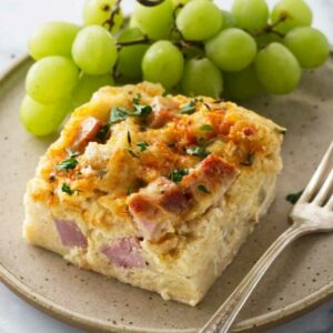 Breakfast casserole slice and green grapes on plate with fork.