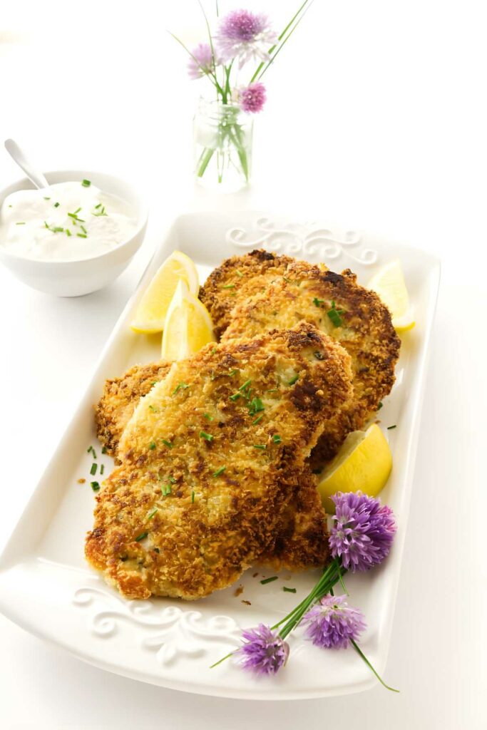 Three breaded fish fillets with chives, lemon wedges, and dipping sauce.