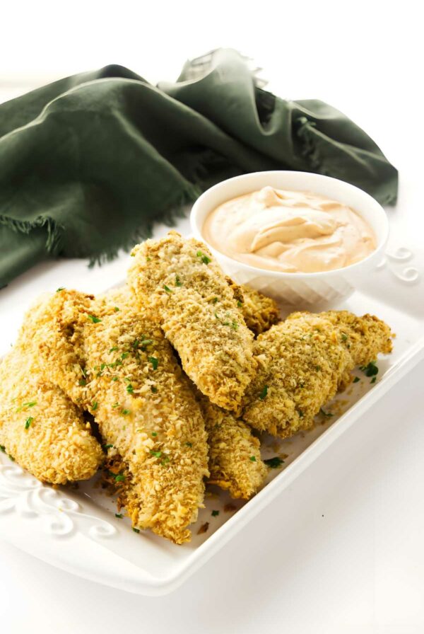 Golden breaded chicken tenders with herbs and creamy dipping sauce on plate.