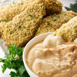 Breaded baked fish with creamy dipping sauce, garnished with parsley.