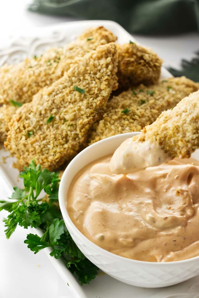 Breaded chicken tenders with creamy dipping sauce, garnished with parsley.