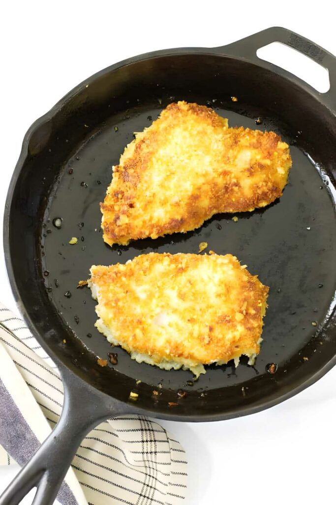 Two breaded chicken cutlets frying in a black skillet.