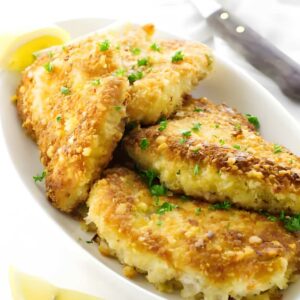 Golden breaded fish fillets with parsley and lemon on a white plate.
