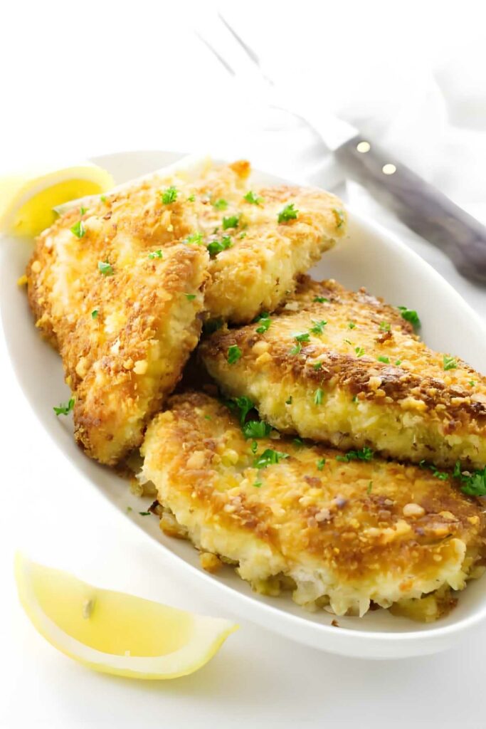 Golden breaded fish fillets with parsley and lemon on a white plate.