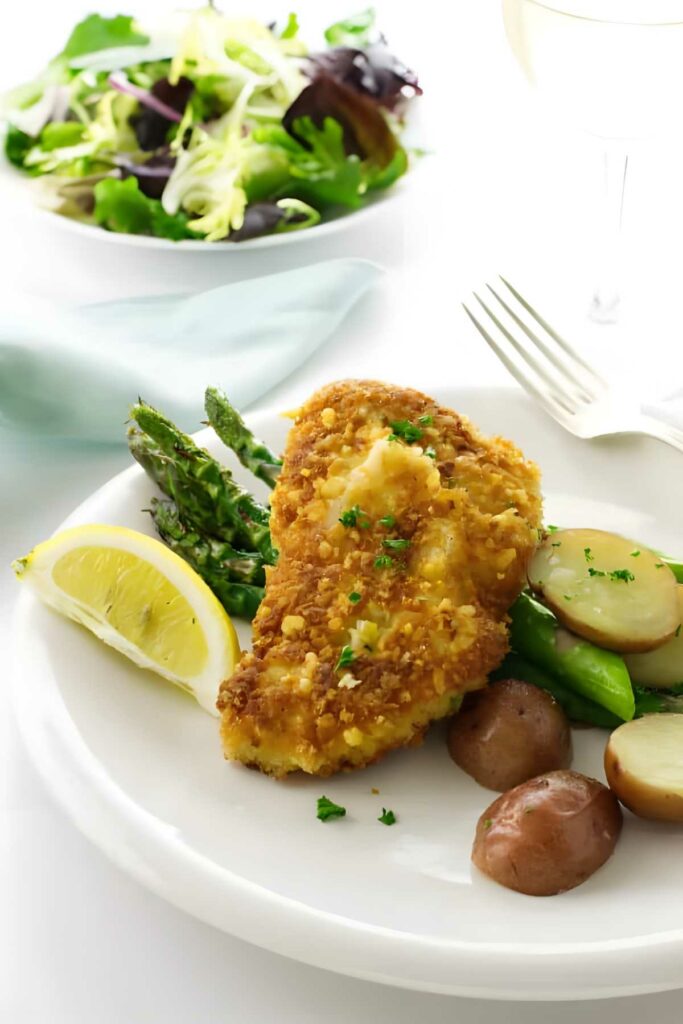 Breaded chicken, asparagus, sliced potatoes, and lemon on a white plate.