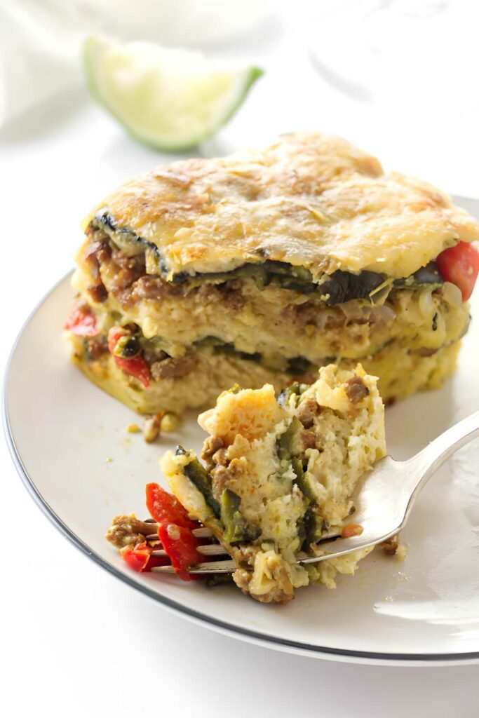 Close-up of cheesy layered breakfast casserole slice with fork holding a piece.