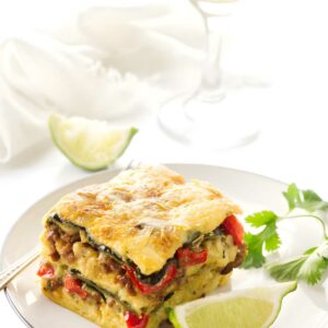 Slice of vegetable and meat lasagna, garnished with cilantro and lime.