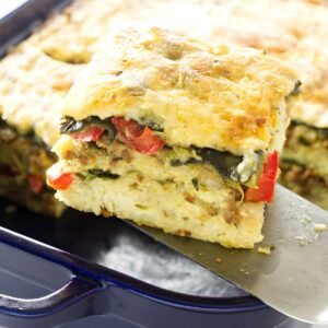 Spatula lifts chorizo strata slice from blue dish, layers visible.
