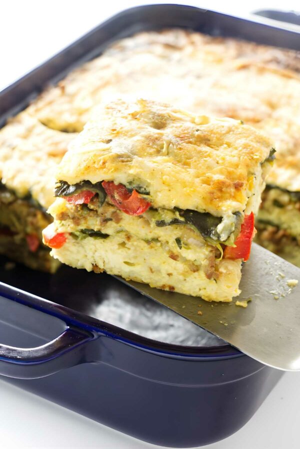 Spatula lifts chorizo strata slice from blue dish, layers visible.