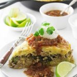 Cornbread casserole slice with salsa, sour cream, cilantro, and lime on a white plate.
