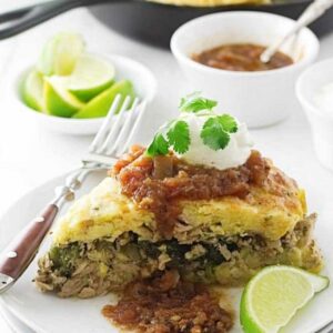 Cornbread casserole slice with salsa, sour cream, cilantro, and lime on a white plate.