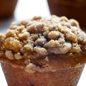 Close-up of a pumpkin muffin with crumbly streusel, two blurred in background.