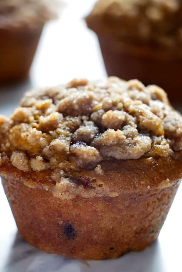 Close-up of a pumpkin muffin with crumbly streusel, two blurred in background.