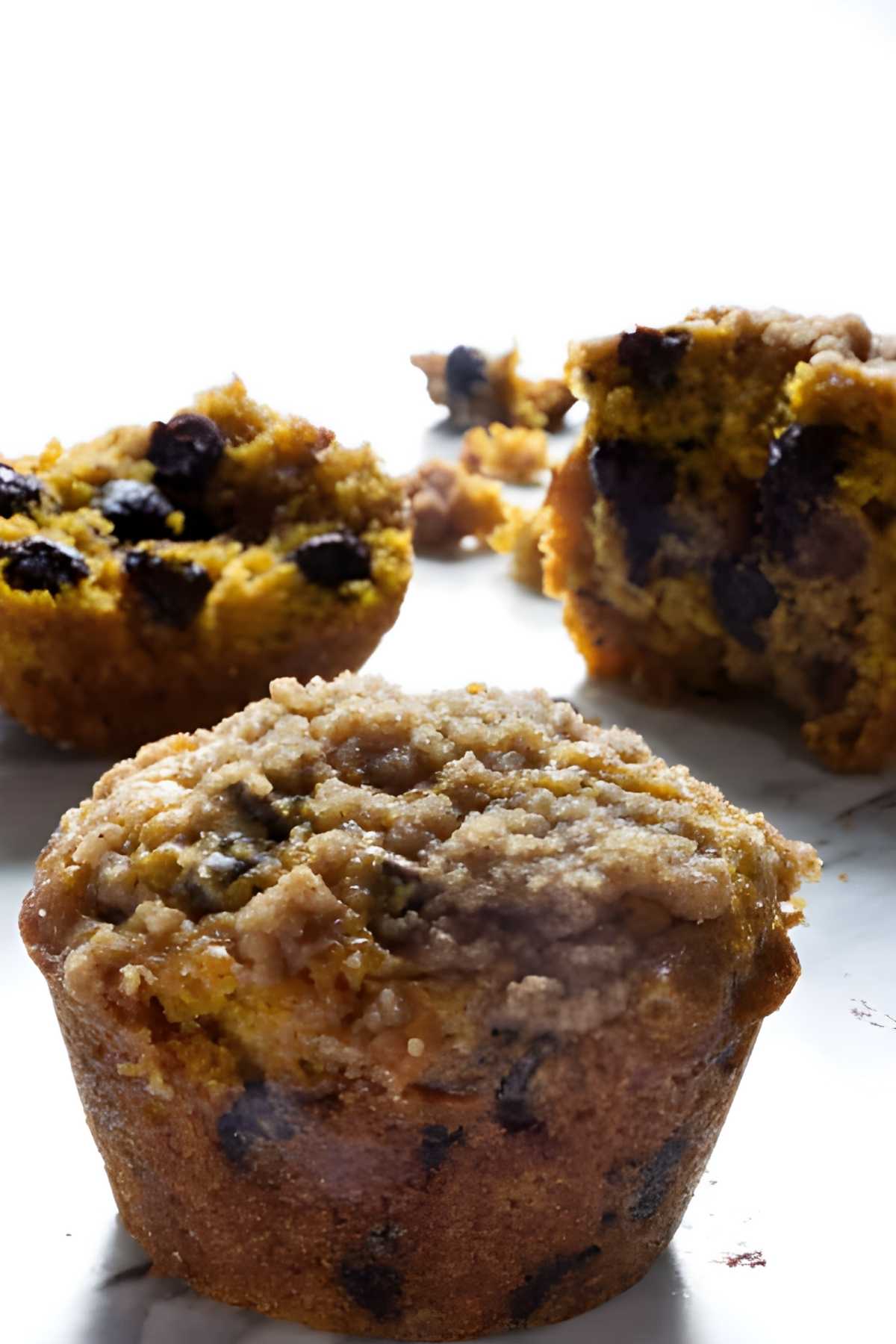 Two pumpkin chocolate chip muffins with streusel topping, one split open.
