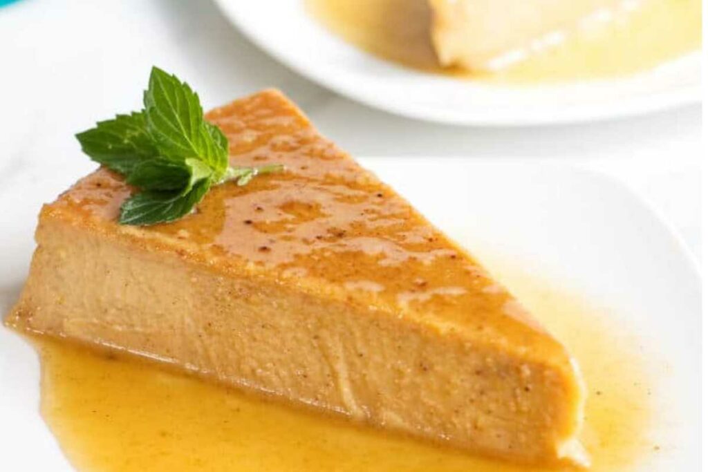 A slice of flan with caramel sauce and mint on a white plate.
