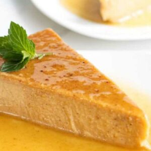A slice of flan with caramel sauce and mint on a white plate.