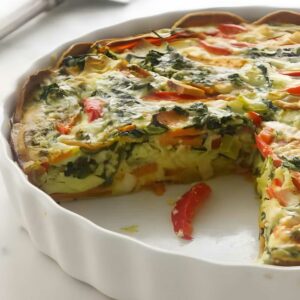 Vegetable quiche with a slice missing in a white ceramic dish.