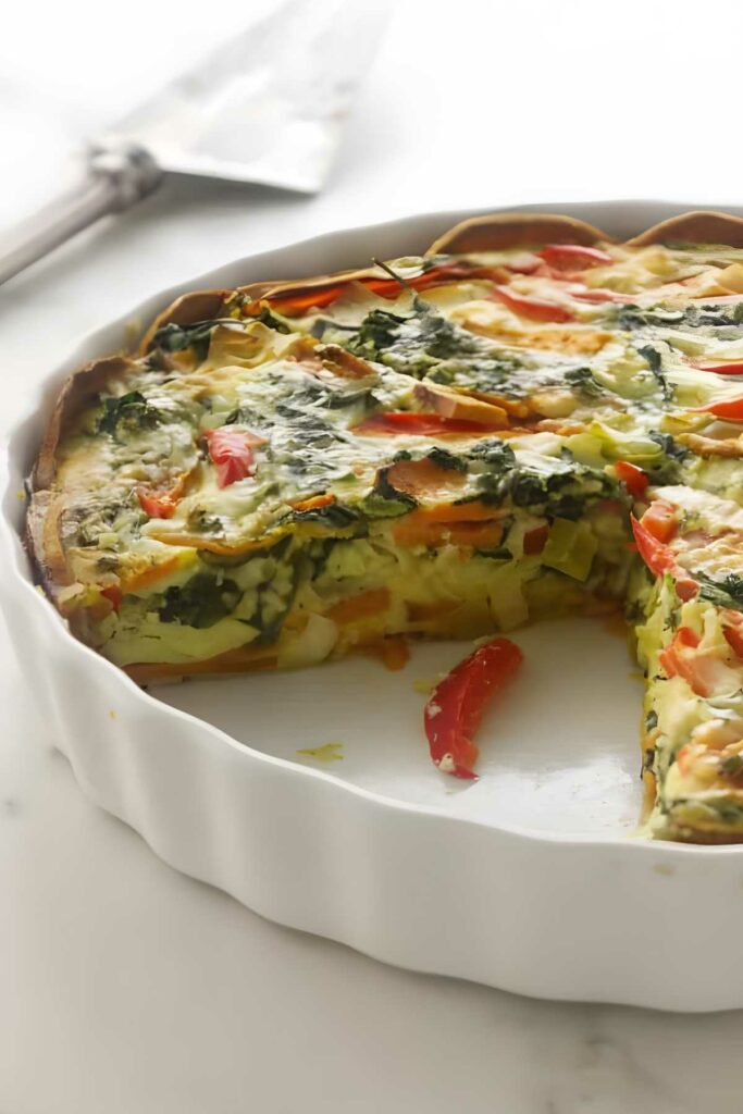 Vegetable quiche with a slice missing in a white ceramic dish.