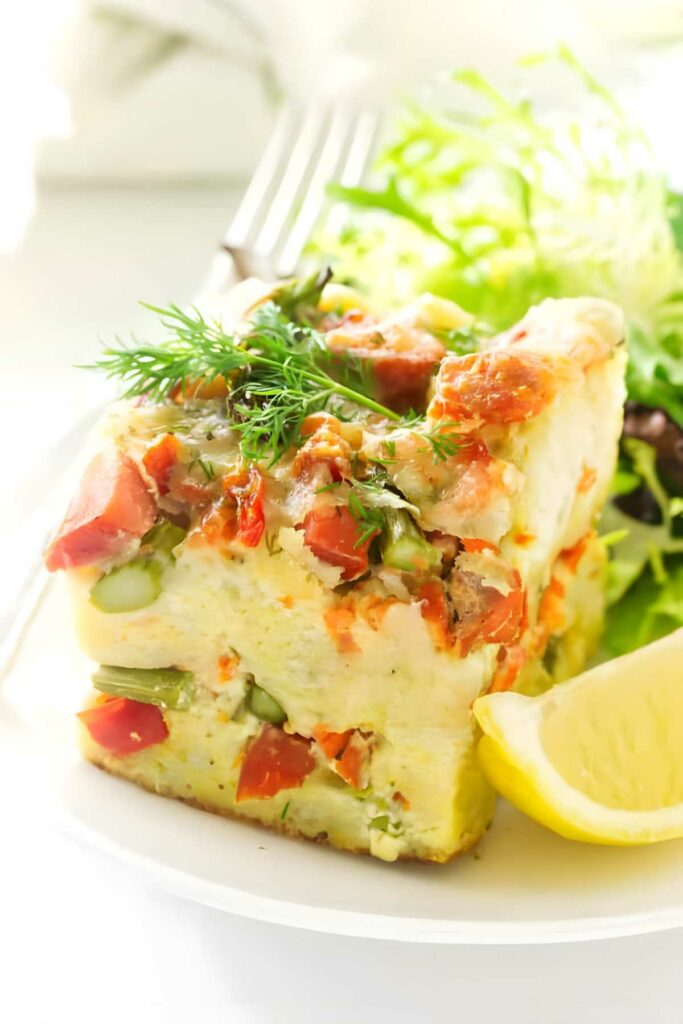 Salmon breakfast strata slice with dill, salad, lemon wedge, and fork.