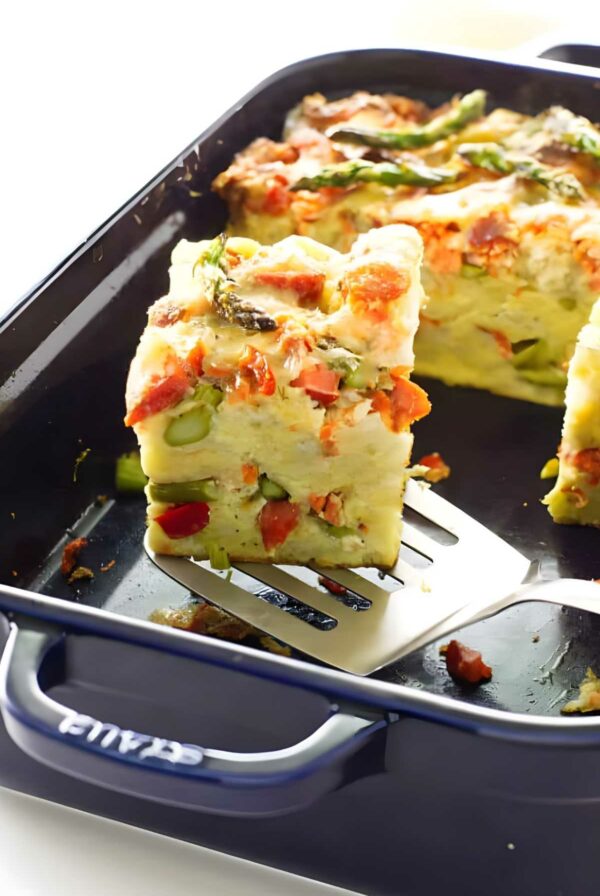 Slice of savory bread pudding with asparagus and red pepper on spatula.