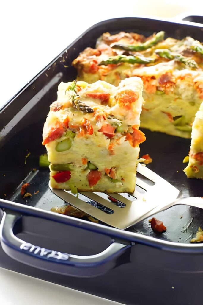 Slice of savory bread pudding with asparagus and red pepper on spatula.