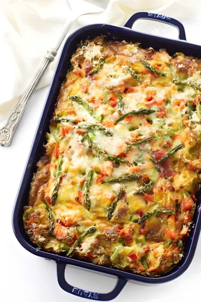 Salmon casserole topped with cheese, asparagus, peppers, in blue dish.