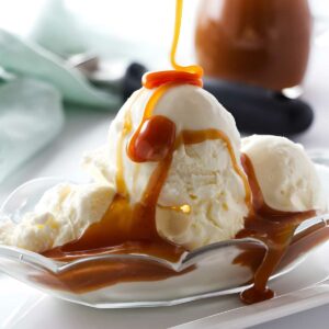 Vanilla ice cream scoops in a dish with caramel sauce being poured.