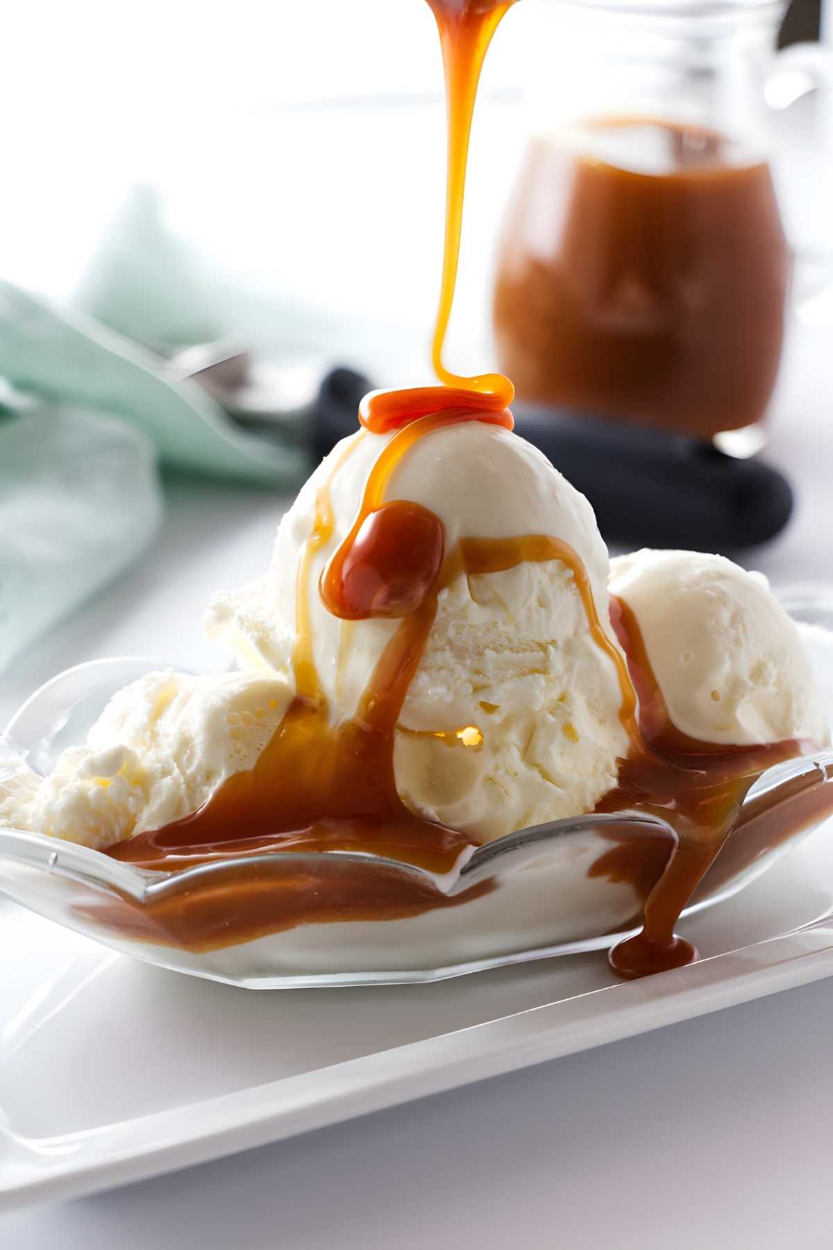 Vanilla ice cream scoops in a dish with caramel sauce being poured.
