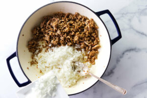 Adding diced onions to the skillet with cooked sausage.