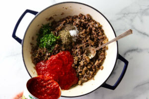 Adding crushed tomatoes in a skillet with ground sausage and spices.