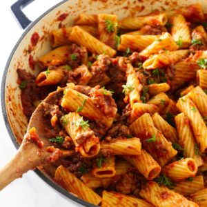 Scooping a serving of sausage rigatoni with a wooden spoon.