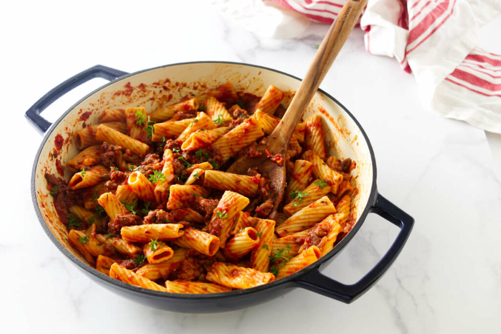 A skillet with sausage and pasta next to a kitchen towel.