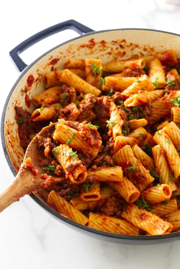 Wooden spoon scooping pasta with sausage sauce.